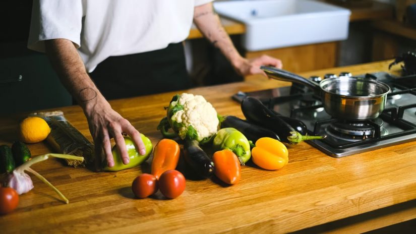 Close-up of a chef arranging fresh vegetables on a wooden kitchen counter for a healthy meal.