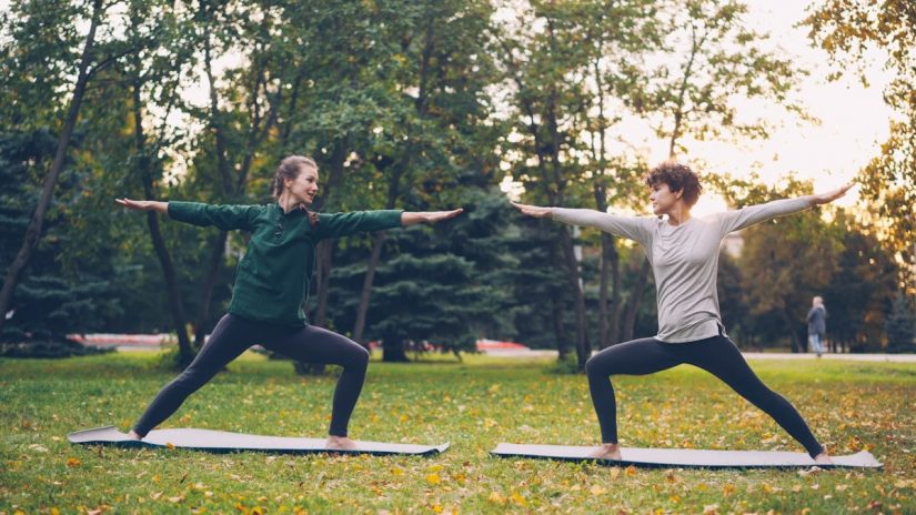 Pretty women is trendy sports clothing are training outdoors doing yoga enjoying movement, fresh air and warm autumn weather. Sports, leisure and youth concept.